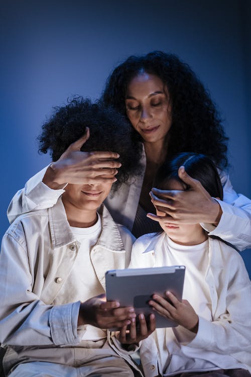 Free Mother covering eyes of her children with hands against internet content on digital pad Stock Photo