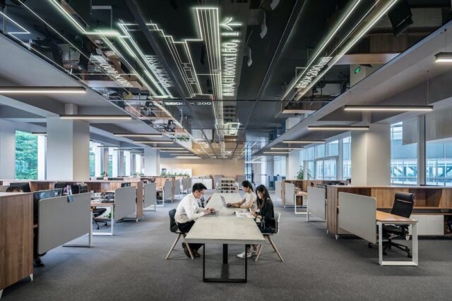 Corporate office with conference table in the middle where three employees discuss resource utilization.