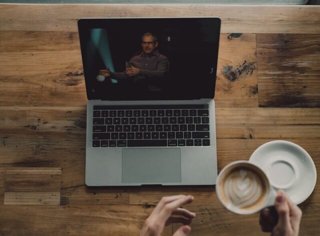 person holding cup of latte while facing MacBook Pro