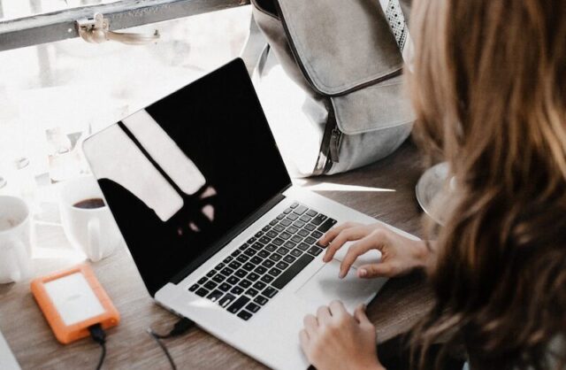 girl wearing grey long-sleeved shirt using MacBook Pro on brown wooden table