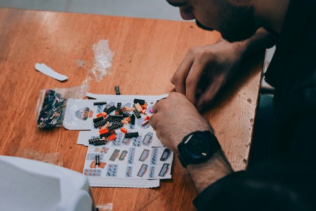 Man assembling small colorful building blocks on a wooden table.